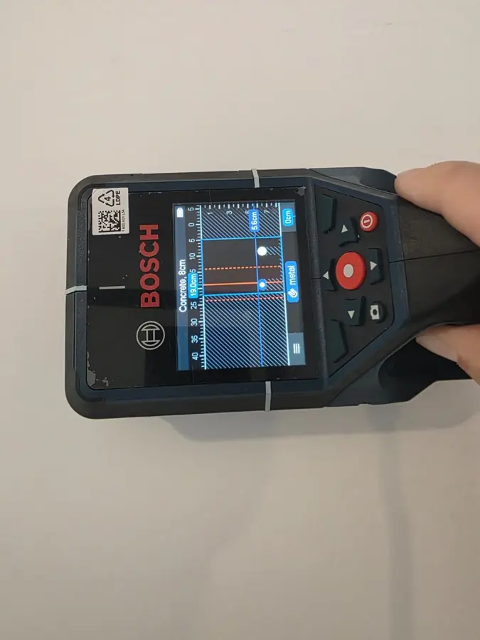 Detector de armături ținut pe un perete, cu armătura vizibilă pe ecran