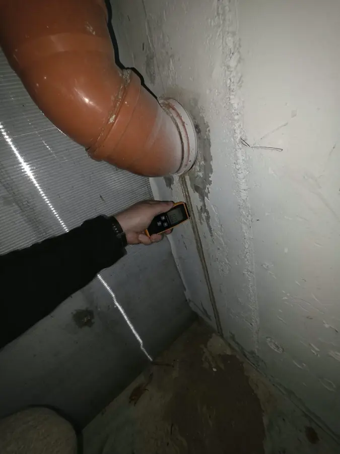 Umidometru ținut pe un perete, sub o țeavă de canalizare